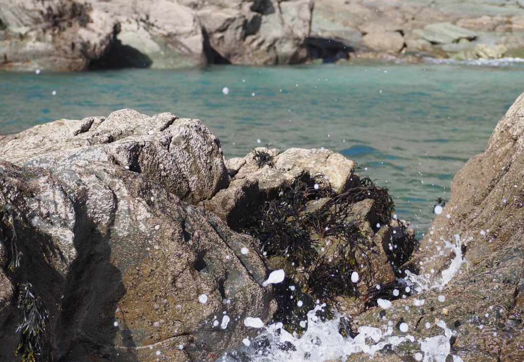 marine spray appears at the base of the image in front of rocks and a tide pool beyond